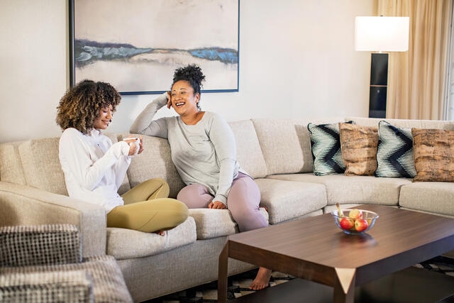 An older woman and younger woman sitting together on a couch in a Hilton Grand Vacations suite.