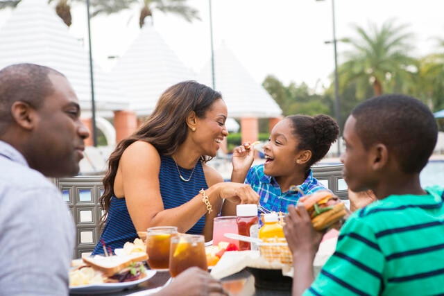 Family enjoying a meal together poolside at Hilton Grand Vacations at SeaWorld resort in Orlando.